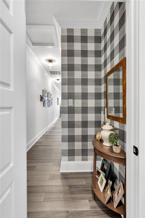 hall with visible vents, wood finished floors, baseboards, and ornamental molding
