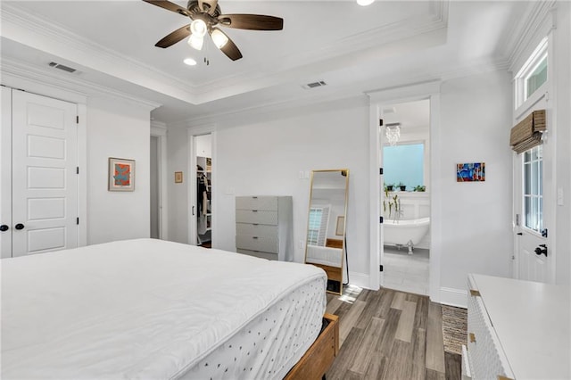 bedroom with a raised ceiling, ornamental molding, wood-type flooring, and a closet