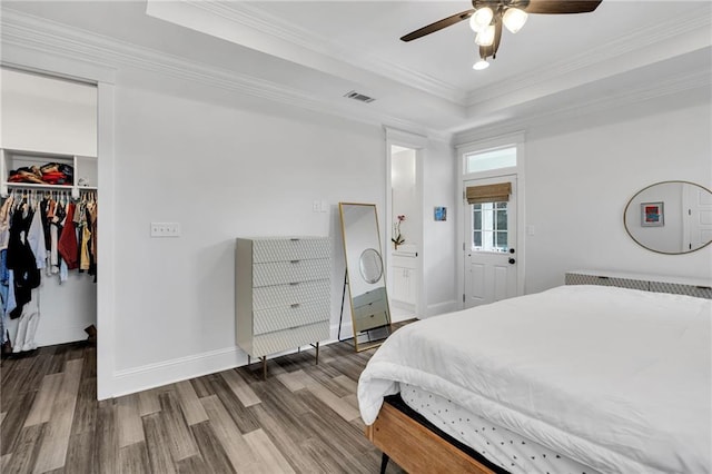 bedroom featuring crown molding, a walk in closet, a tray ceiling, a closet, and hardwood / wood-style floors