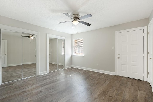 unfurnished bedroom featuring multiple closets, ceiling fan, a textured ceiling, and dark hardwood / wood-style flooring