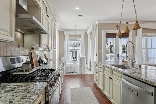 kitchen with sink, appliances with stainless steel finishes, light stone countertops, cream cabinetry, and wall chimney exhaust hood