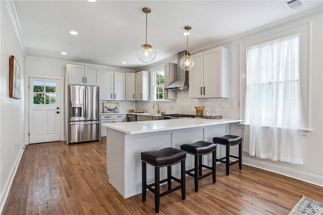 kitchen featuring stainless steel appliances, decorative light fixtures, kitchen peninsula, and wall chimney range hood