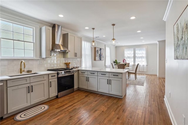 kitchen featuring pendant lighting, wall chimney range hood, sink, stainless steel appliances, and kitchen peninsula