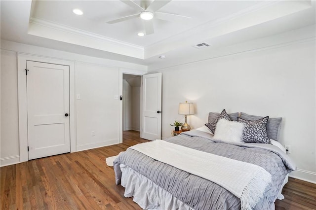 bedroom with wood-type flooring, ornamental molding, ceiling fan, and a tray ceiling