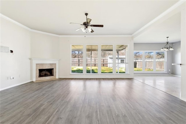 unfurnished living room featuring a tiled fireplace, crown molding, ceiling fan with notable chandelier, and wood-type flooring