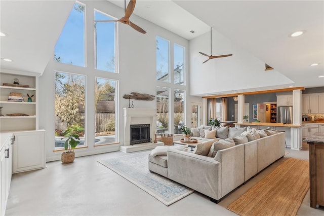 living area featuring a fireplace with raised hearth, concrete flooring, recessed lighting, a high ceiling, and a ceiling fan