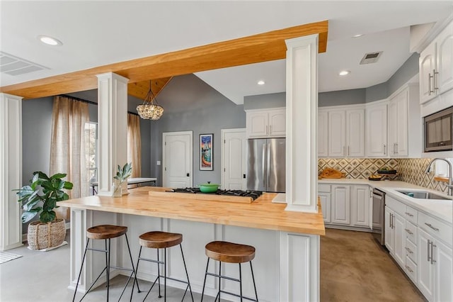 kitchen with butcher block counters, a sink, white cabinetry, appliances with stainless steel finishes, and decorative columns