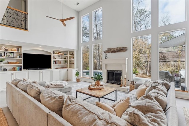 living room with built in shelves, a fireplace with raised hearth, visible vents, and a ceiling fan