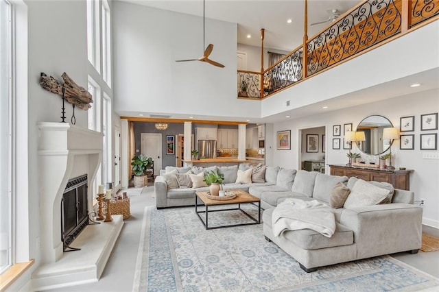 living area featuring a towering ceiling, a glass covered fireplace, a ceiling fan, and recessed lighting