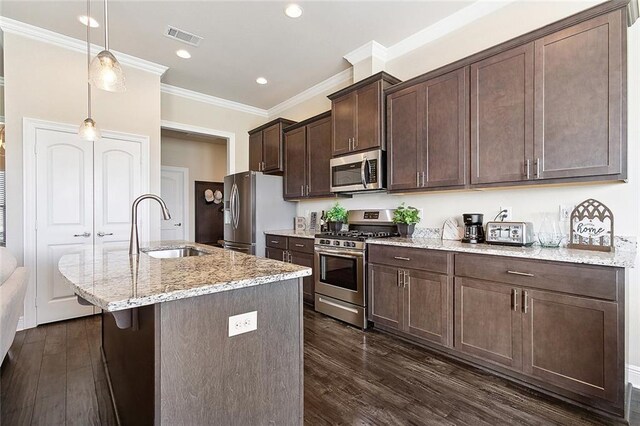 kitchen with sink, a kitchen island with sink, stainless steel appliances, light stone countertops, and decorative light fixtures