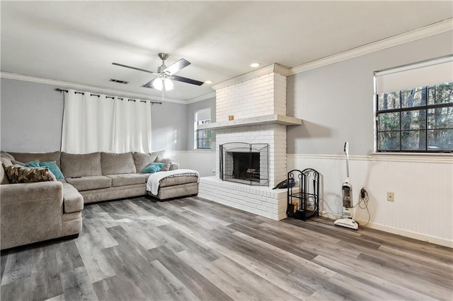 living room featuring hardwood / wood-style flooring, ceiling fan, ornamental molding, and a fireplace