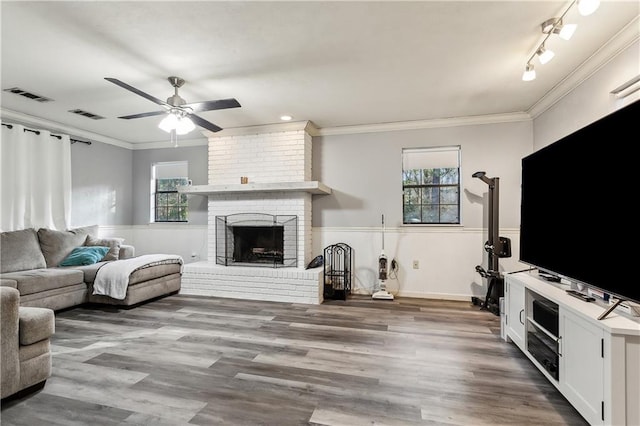 living room with crown molding, light hardwood / wood-style floors, a brick fireplace, and a wealth of natural light