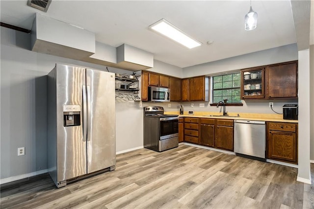 kitchen with hanging light fixtures, stainless steel appliances, sink, and light wood-type flooring