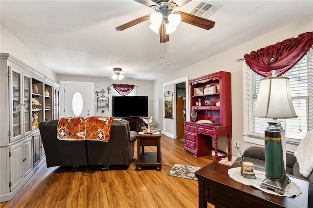 living room with ceiling fan, visible vents, and wood finished floors