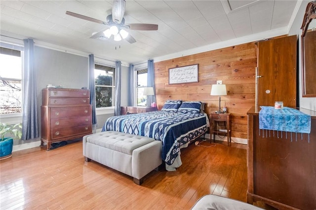 bedroom featuring ceiling fan, ornamental molding, light hardwood / wood-style flooring, and wood walls