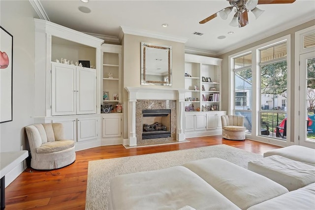 sitting room featuring crown molding, ceiling fan, a fireplace, built in shelves, and light wood-type flooring