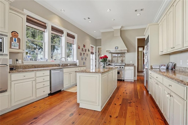 kitchen with wall chimney range hood, stainless steel appliances, a center island, light stone counters, and light wood-type flooring