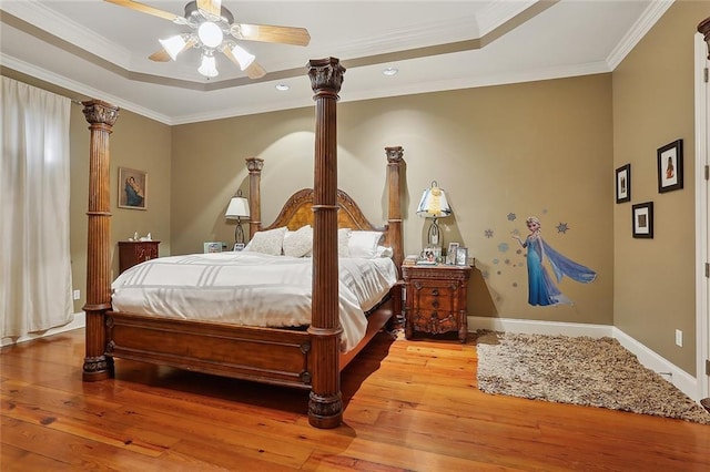 bedroom featuring decorative columns, wood-type flooring, ornamental molding, ceiling fan, and a tray ceiling