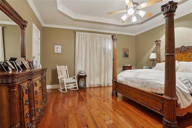 bedroom featuring decorative columns, wood-type flooring, ornamental molding, and a tray ceiling