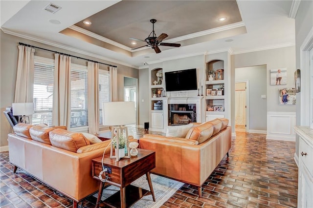 living room with built in shelves, ornamental molding, a raised ceiling, and ceiling fan