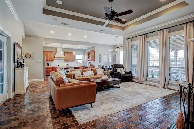 living room with a tray ceiling, ceiling fan with notable chandelier, and ornamental molding