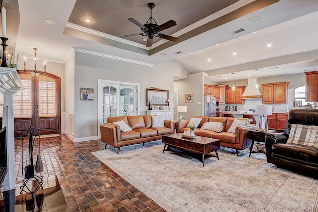 living room featuring french doors, crown molding, a raised ceiling, and ceiling fan with notable chandelier