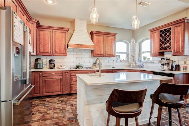 kitchen with premium range hood, appliances with stainless steel finishes, a kitchen breakfast bar, and a kitchen island with sink