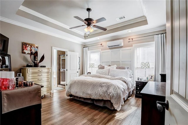 bedroom with a raised ceiling, crown molding, hardwood / wood-style flooring, and a wall mounted air conditioner