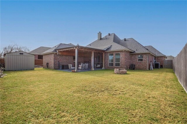 back of house with a storage shed, an outdoor fire pit, a lawn, and a patio area