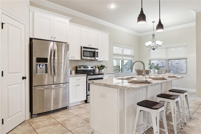 kitchen with pendant lighting, appliances with stainless steel finishes, a kitchen island with sink, white cabinetry, and light stone countertops