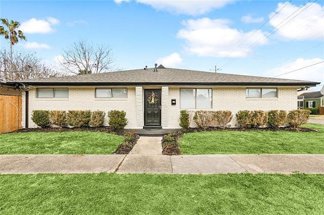 ranch-style house featuring brick siding, roof with shingles, a front lawn, and fence