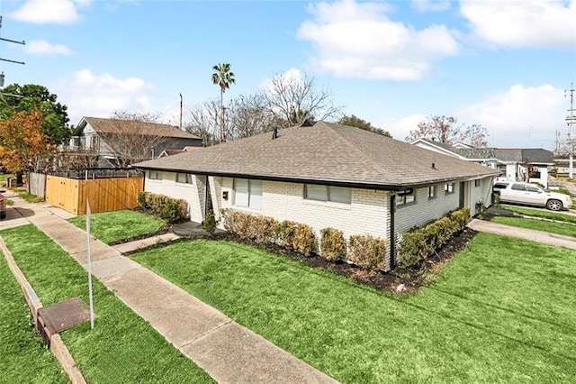 view of side of property with a yard, brick siding, roof with shingles, and fence