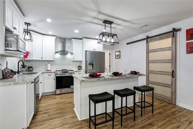 kitchen featuring white cabinetry, stainless steel appliances, a kitchen island, a barn door, and wall chimney exhaust hood