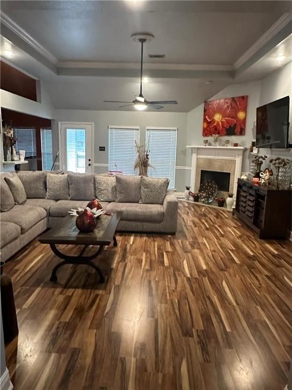 living room with ornamental molding, a tray ceiling, ceiling fan, a tiled fireplace, and hardwood / wood-style floors