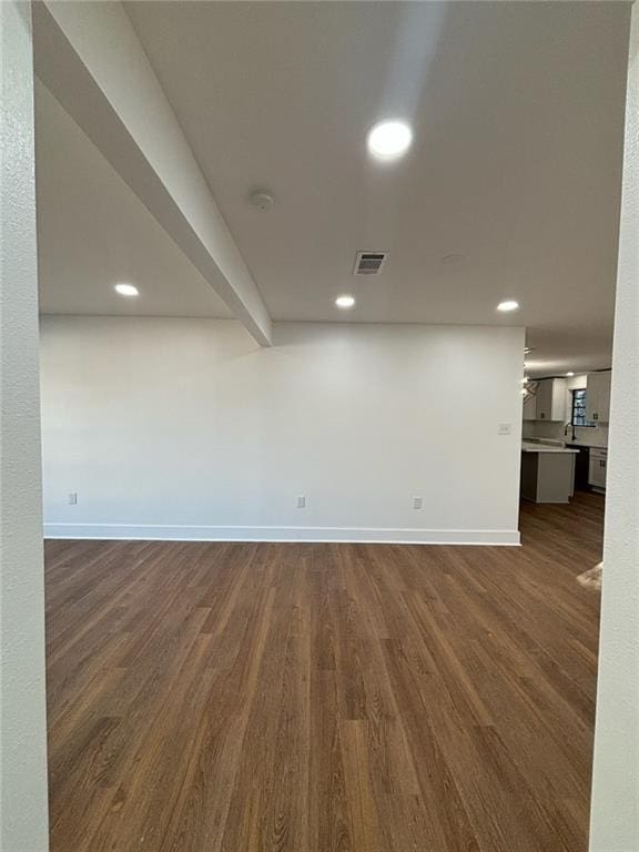 spare room featuring beamed ceiling and dark wood-type flooring