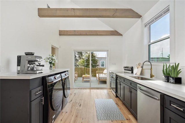 kitchen featuring sink, appliances with stainless steel finishes, lofted ceiling with beams, washing machine and clothes dryer, and light wood-type flooring