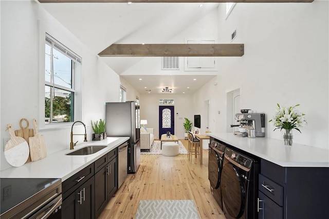 kitchen featuring sink, light hardwood / wood-style floors, stainless steel appliances, washing machine and dryer, and beam ceiling