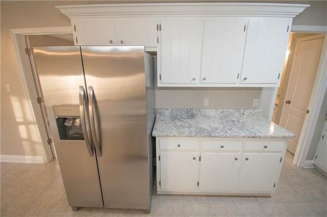 kitchen with light stone counters, light tile patterned flooring, stainless steel fridge with ice dispenser, and white cabinets