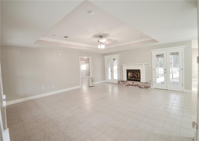 unfurnished living room featuring crown molding, a brick fireplace, a tray ceiling, and french doors