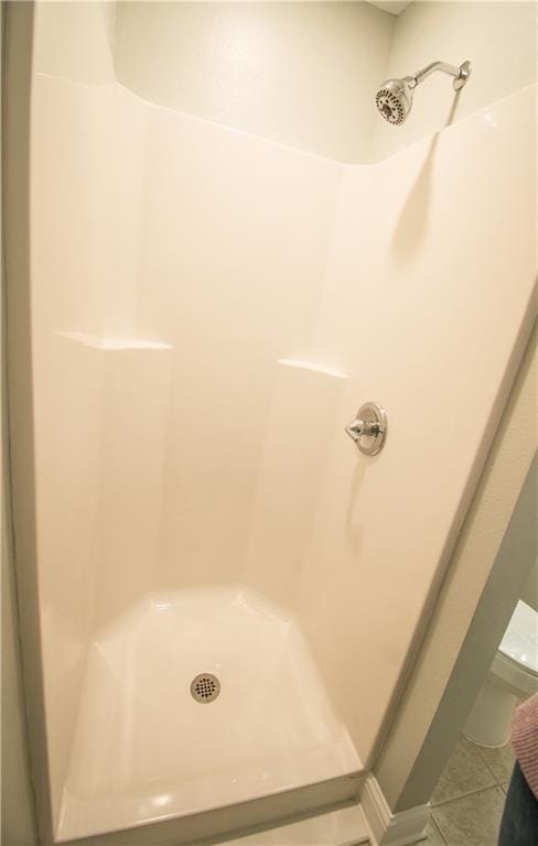 bathroom featuring tile patterned flooring, toilet, and a shower