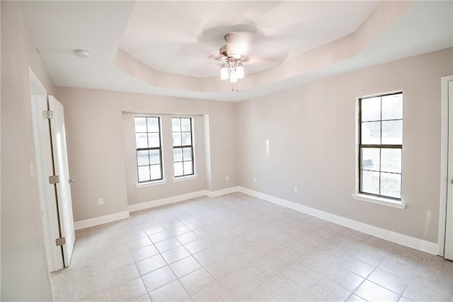 empty room with light tile patterned floors, ceiling fan, and a tray ceiling