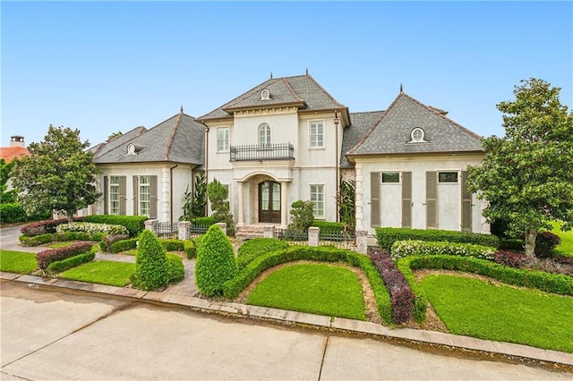 french provincial home with french doors, a balcony, and a front yard