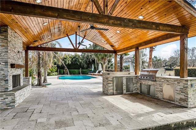 view of patio / terrace featuring area for grilling, an outdoor stone fireplace, exterior kitchen, ceiling fan, and a gazebo