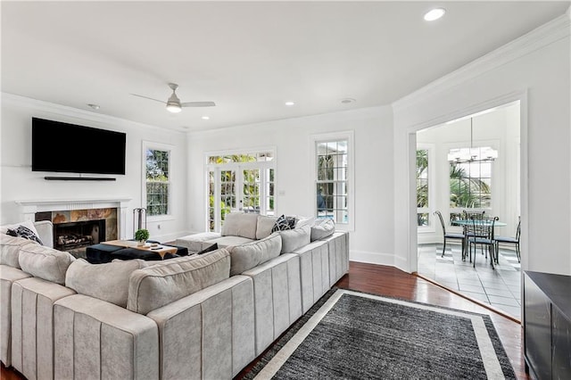 living room with hardwood / wood-style flooring, ornamental molding, a premium fireplace, and ceiling fan with notable chandelier