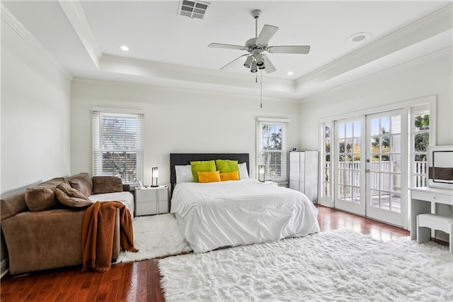 bedroom with dark wood-type flooring, a tray ceiling, multiple windows, and access to outside