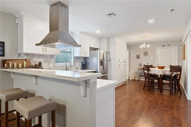 kitchen with a breakfast bar area, white cabinetry, stainless steel fridge with ice dispenser, kitchen peninsula, and island exhaust hood