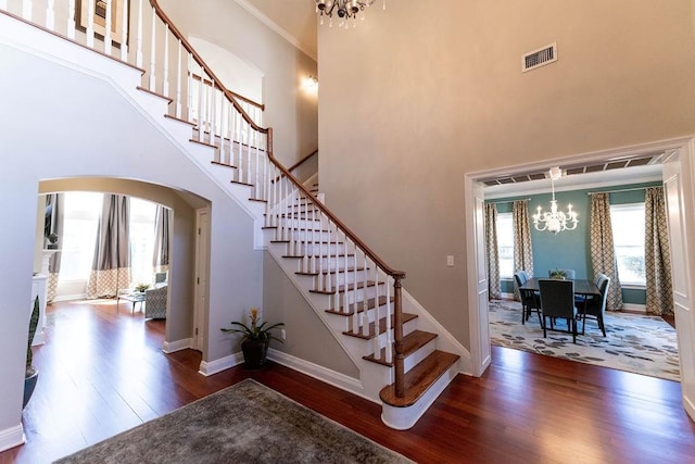 stairway with hardwood / wood-style flooring, crown molding, a high ceiling, and a chandelier