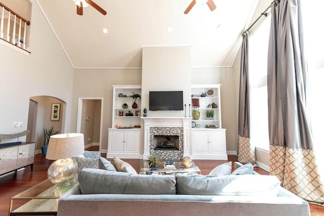 living room with crown molding, dark wood-type flooring, a tile fireplace, ceiling fan, and high vaulted ceiling