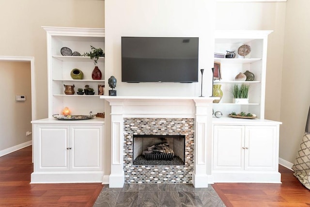 living room featuring a tiled fireplace, dark wood-style floors, built in features, and baseboards