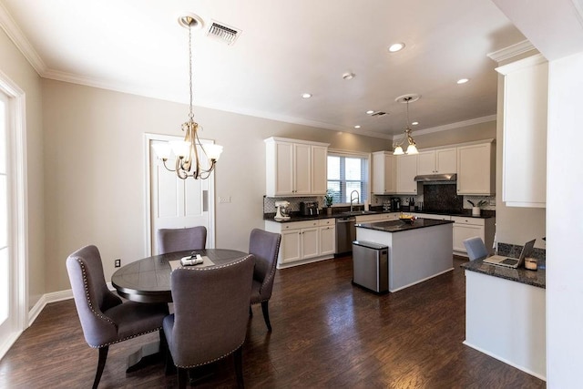 dining room with dark wood-type flooring, ornamental molding, sink, and a notable chandelier